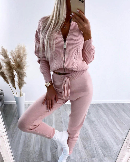 Frau in rosa Strick-Set mit Reißverschluss, posiert vor Spiegel. Modetrend, gemütlicher Look, Indoor-Fashion, elegantes Freizeitoutfit.