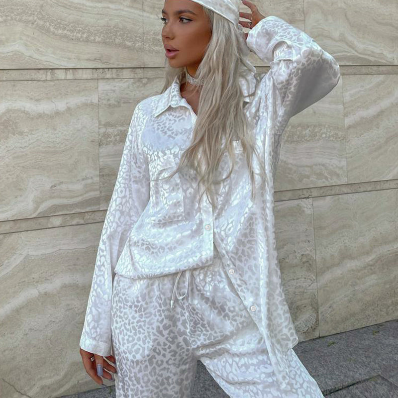 Frau in weißem Satin-Pyjama mit Leopardenmuster vor beiger Steinwand. Modetrend, Nachtwäsche, eleganter Look.