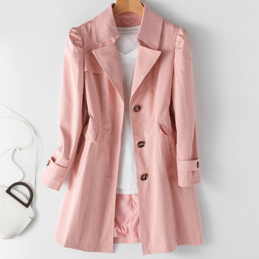 Rosa Damen-Trenchcoat aus Baumwolle, hängend auf Holzkleiderbügel, mit weißen T-Shirt darunter. Elegante Mode für Frühling und Herbst.