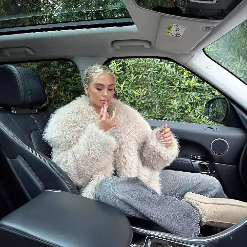 Frau im Auto mit beigem Pelzmantel, trägt Lippenstift auf. Luxuriöses Interieur, grüne Pflanzen im Hintergrund. Eleganz, Mode, Autofahrt.