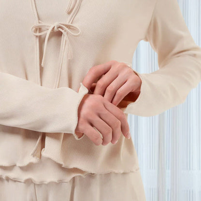 Frau in beigem, geripptem Pyjama-Set mit Kordelzug, weichem Stoff und langen Ärmeln. Komfortable Nachtwäsche, modisch und gemütlich.