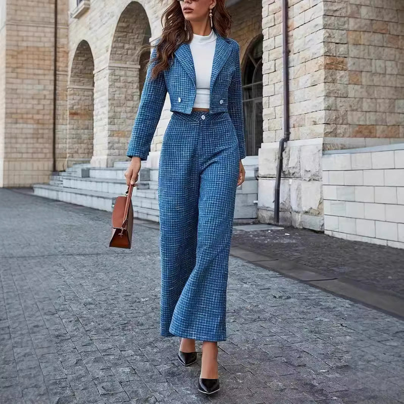 Frau in blauem Hosenanzug und weißem Oberteil, trägt braune Handtasche, geht auf gepflastertem Weg vor historischer Steinarchitektur.