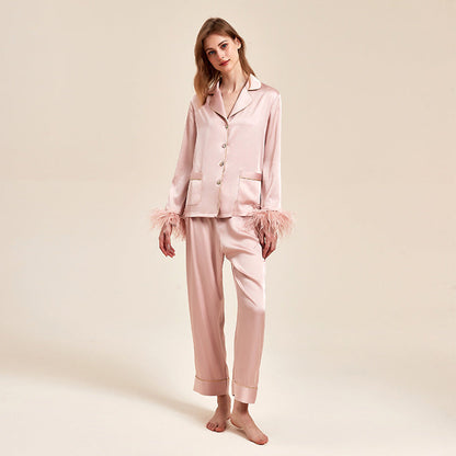 Frau in eleganter rosa Seidenpyjama mit Federdetails, stehend vor neutralem Hintergrund. Luxuriöse Nachtwäsche, modisch, bequem.