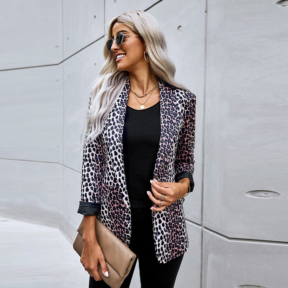 Frau mit Sonnenbrille trägt Leopardenmuster-Blazer, schwarze Kleidung und hält eine beige Clutch vor moderner Betonwand. Fashion, Streetstyle, Mode.