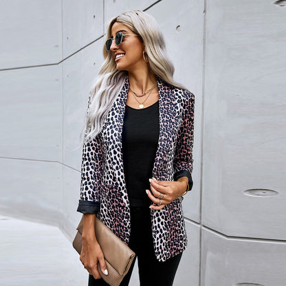 Frau mit Sonnenbrille trägt Leopardenmuster-Blazer, schwarze Kleidung und hält eine beige Clutch vor moderner Betonwand. Fashion, Streetstyle, Mode.