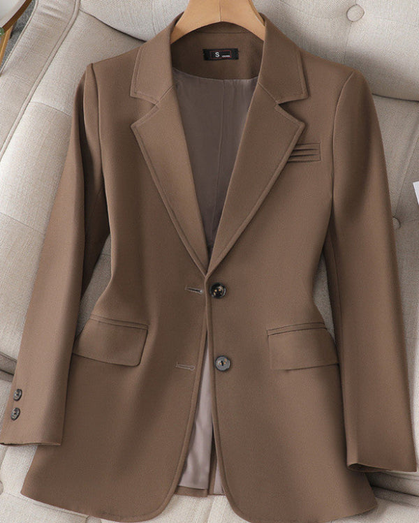 Brauner Damenblazer auf einem beigen Sessel, klassischer Schnitt mit zwei Knöpfen, Reverskragen und Pattentaschen. Elegante Businessmode.