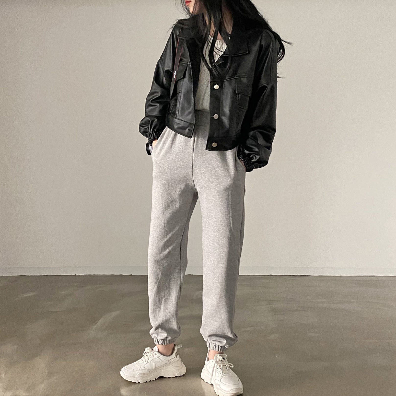 Frau in schwarzer Lederjacke und grauer Jogginghose, weiße Sneaker, modischer Streetstyle, lässiges Outfit, minimalistische Mode.