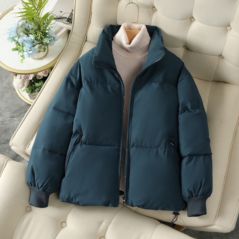 Dunkelblaue Daunenjacke auf cremefarbenem Sofa, mit Reißverschluss und Stehkragen. Wintermode, warme Oberbekleidung, stilvoll und gemütlich.