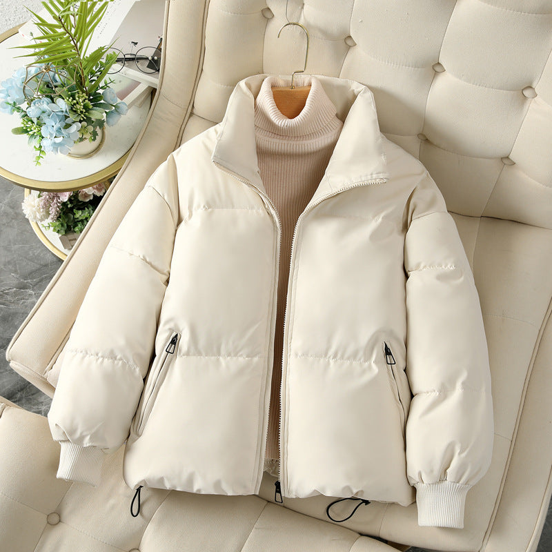 Beige Daunenjacke auf cremefarbenem Sessel, Reißverschluss, Stehkragen, modisch, warm, Wintermode, Damenbekleidung, gemütlich, stilvoll.