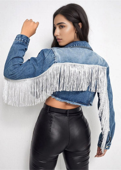 Frau in blauer Jeansjacke mit weißen Fransen, schwarze Lederhose, seitlich stehend. Modetrend, Damenbekleidung, Fransenjacke.