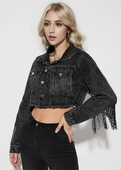 Junge Frau in schwarzer, fransiger Jeansjacke und schwarzer Hose vor weißem Hintergrund. Modetrend, Damenbekleidung, Streetwear.