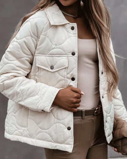 Dame in beiger, gesteppter Jacke mit Knopfleiste und Brusttasche, kombiniert mit beigem Top und Hose. Modetrend Herbst, stilvolle Damenbekleidung.
