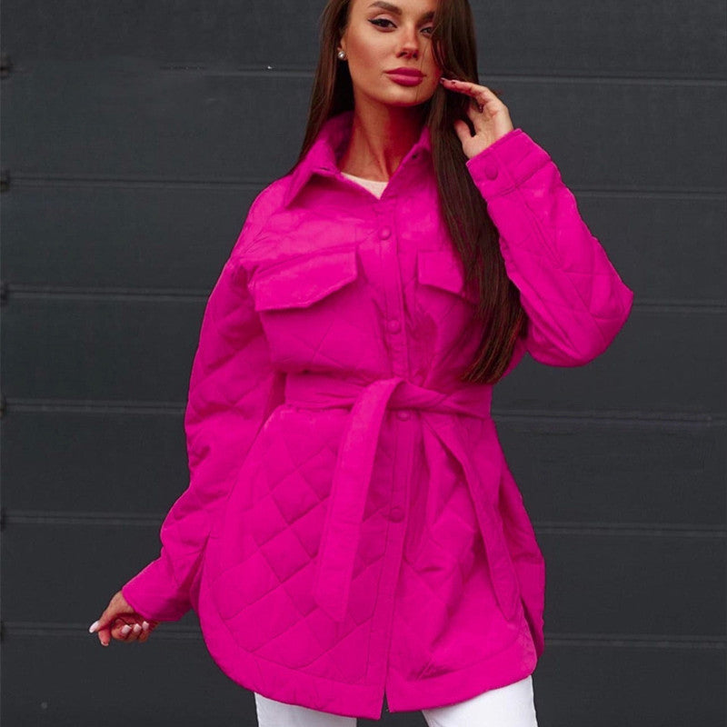 Frau in leuchtend pinker, gesteppter Jacke mit Gürtel vor schwarzem Hintergrund. Modetrend, Damenbekleidung, Herbstmode.