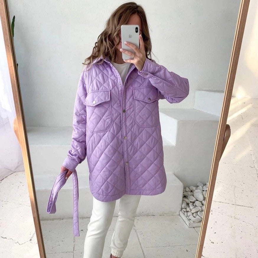 Frau in lila Steppjacke macht Selfie im Spiegel. Modetrend, Winterjacke, Freizeitkleidung. Helle, minimalistische Umgebung.