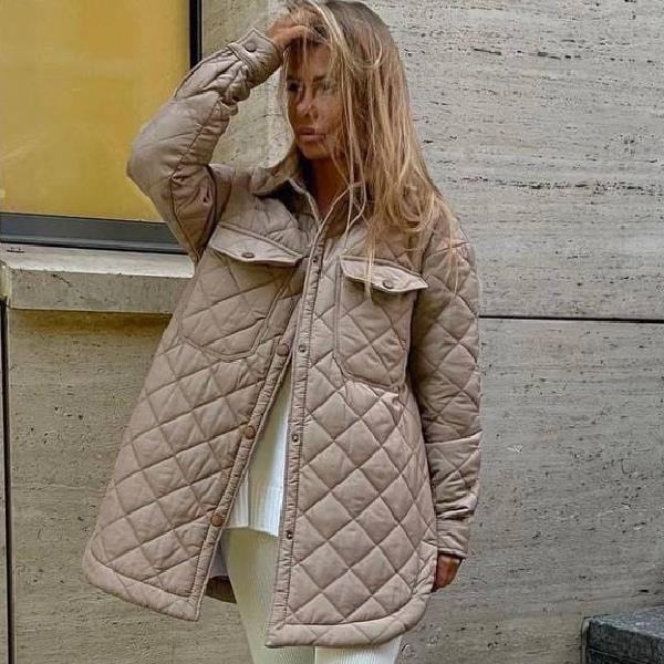 Frau in beiger, gesteppter Jacke vor Betonwand, modischer Herbstlook, warme Oberbekleidung, urbaner Stil, trendige Damenmode.