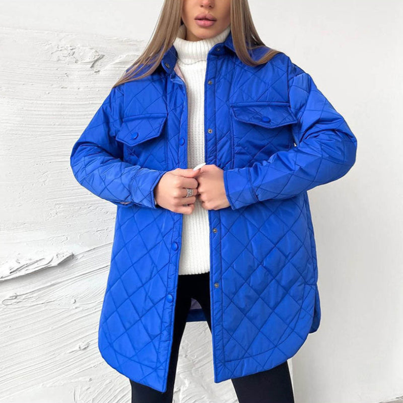 Frau in blauer Steppjacke, weißem Rollkragenpullover und schwarzer Hose vor weißer Wand. Modetrend, Wintermode, Damenbekleidung.