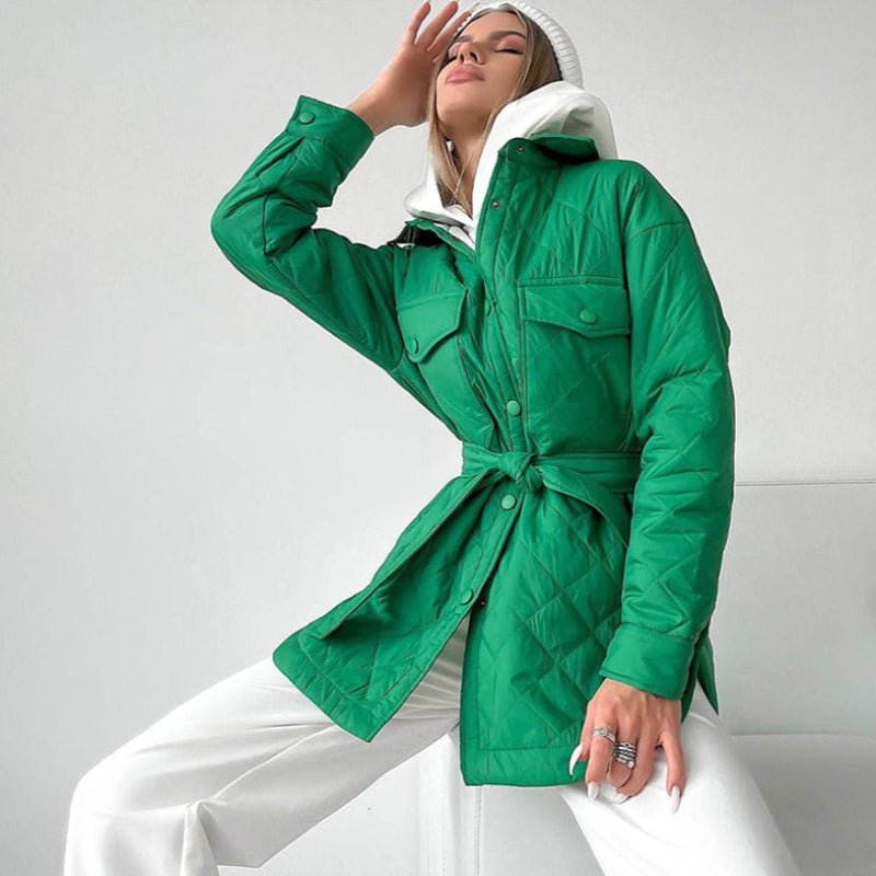 Frau in grüner Steppjacke, weißem Hoodie und Hose posiert modisch. Trendige Wintermode, stilvolle Damenbekleidung, Outdoor-Outfit.