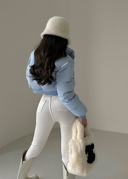 Frau in blauer Daunenjacke, weißer Hose und Stiefeln, hält flauschige Tasche. Wintermode, stilvoller Look, modische Kleidung.