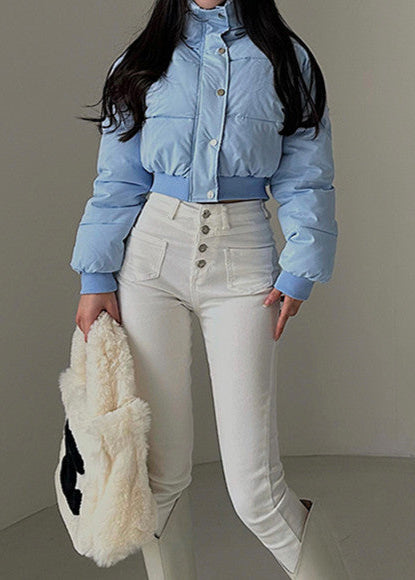 Dame in hellblauer Daunenjacke und weißer High-Waist-Hose, hält eine flauschige Tasche. Modetrend Winter 2023, stilvolle Damenbekleidung.