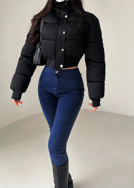 Frau in schwarzer Steppjacke und blauer Jeans, modisch gekleidet, mit schwarzer Handtasche. Wintermode, Damenbekleidung, trendiger Look.