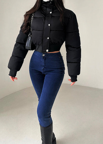 Frau in schwarzer Steppjacke und blauer Jeans, modisch gekleidet, mit schwarzer Handtasche. Wintermode, Damenbekleidung, trendiger Look.