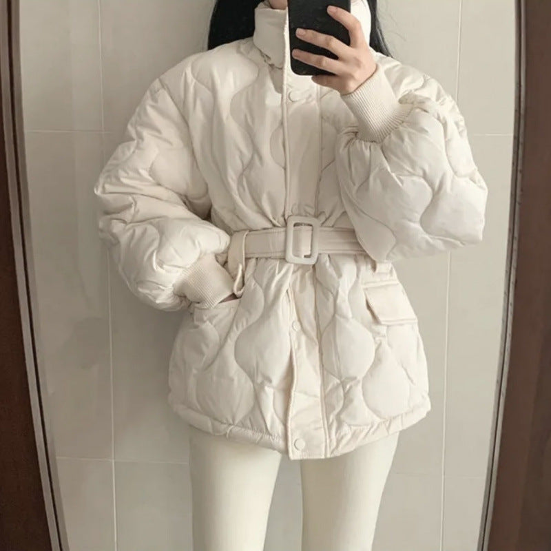 Frau in weißer, gesteppter Daunenjacke mit Gürtel, hält Smartphone vor Spiegel. Wintermode, warme Jacke, modisches Outfit, Selfie.