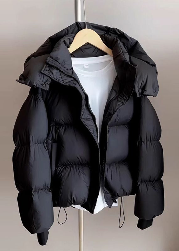 Schwarze Daunenjacke mit Kapuze auf Kleiderbügel, über weißem T-Shirt. Wintermode, warme Oberbekleidung, stilvolle Pufferjacke.