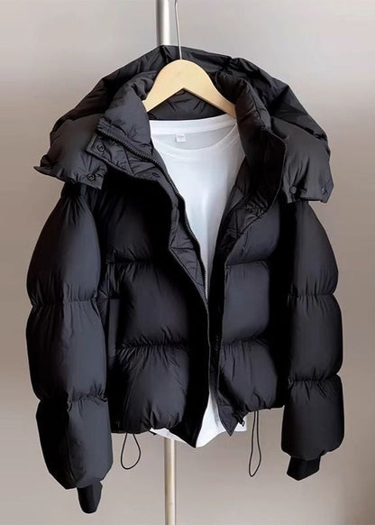 Schwarze Daunenjacke mit Kapuze auf Kleiderbügel, über weißem T-Shirt. Wintermode, warme Oberbekleidung, stilvolle Pufferjacke.