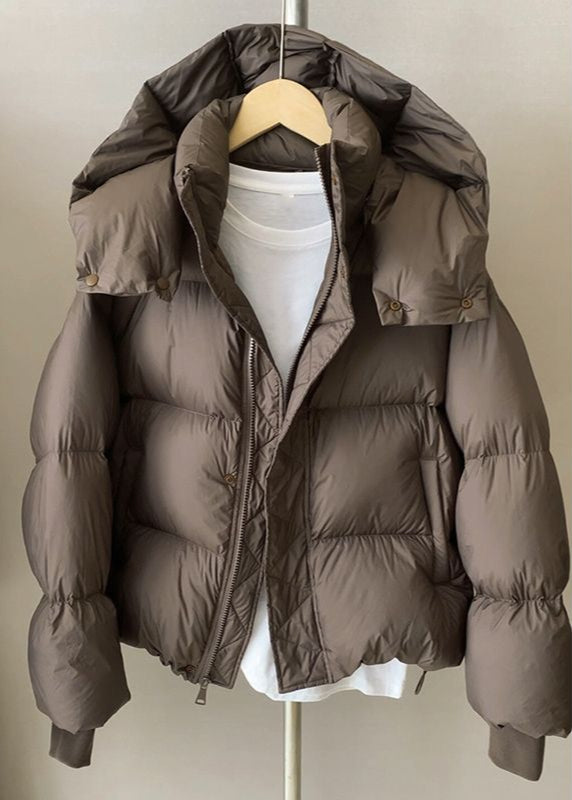 Braune Daunenjacke mit Kapuze auf Kleiderbügel, über weißem T-Shirt. Wintermode, warme Oberbekleidung, stilvolle Outdoor-Bekleidung.