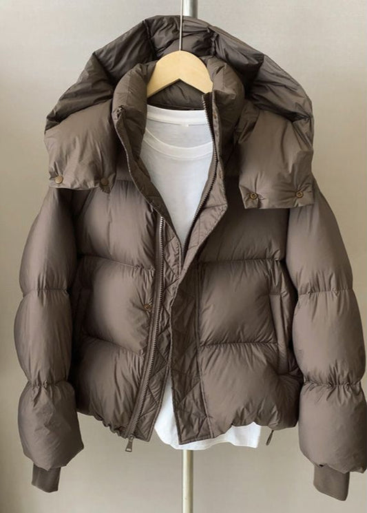 Braune Daunenjacke mit Kapuze auf Kleiderbügel, über weißem T-Shirt. Wintermode, warme Oberbekleidung, stilvolle Outdoor-Bekleidung.