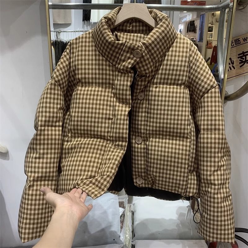 Braune karierte Daunenjacke auf Kleiderbügel, modisch und warm, ideal für Wintermode. Hochwertige Materialien, stilvolles Design, Damenbekleidung.