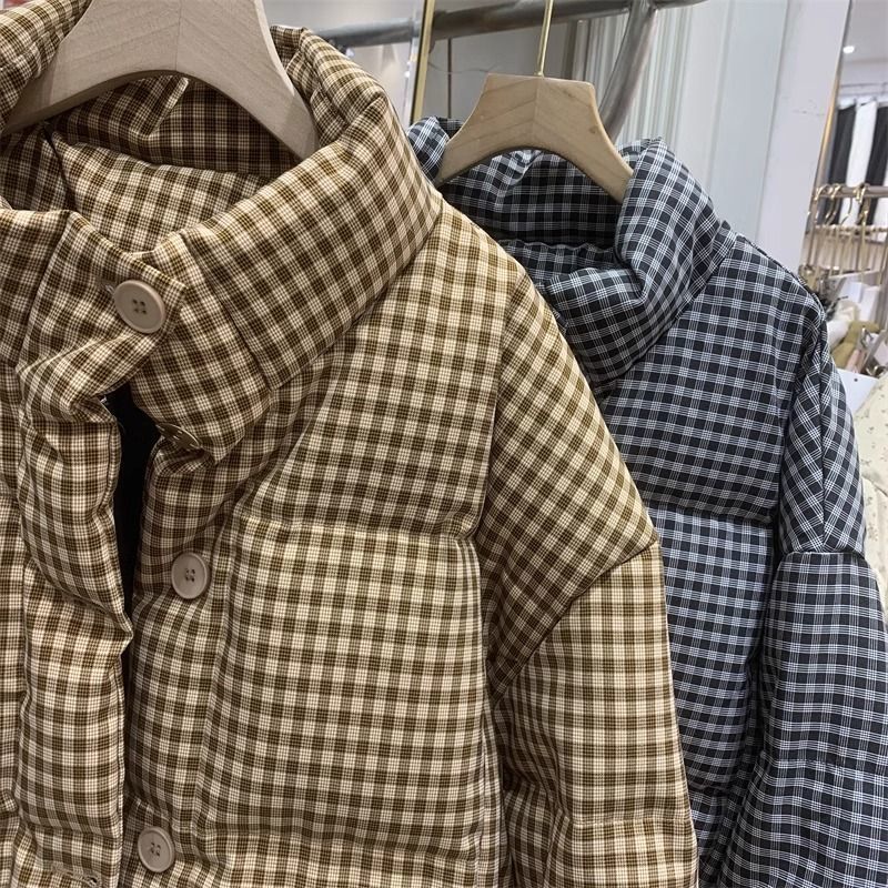 Zwei karierte Daunenjacken, eine in Braun und eine in Blau, hängen auf Holzkleiderbügeln. Modetrend, Winterjacken, kariertes Muster.