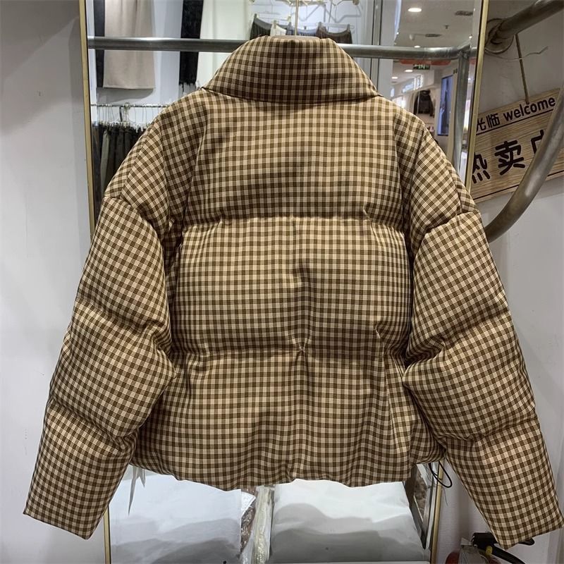 Braune karierte Daunenjacke auf Kleiderbügel, modisch und warm, ideal für Wintermode. Hochwertige Materialien, stilvolles Design, trendige Winterbekleidung.