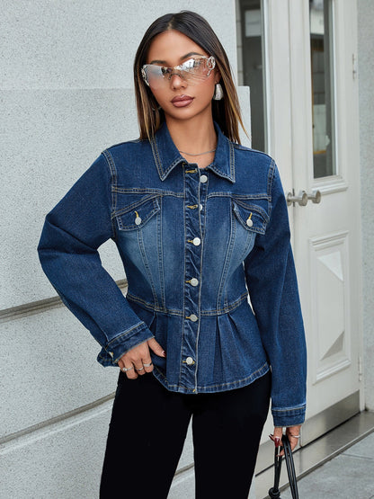 Frau in modischer Jeansjacke, trägt stilvolle Sonnenbrille, steht vor grauer Wand. Trendige Damenmode, urbaner Look, Streetstyle-Outfit.