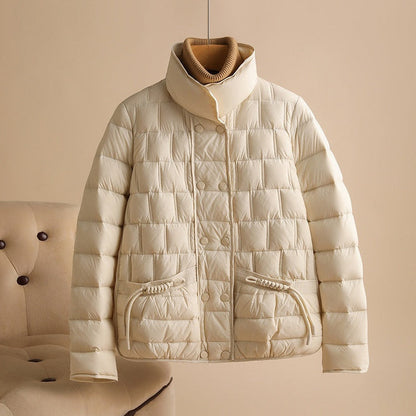 Beige Daunenjacke mit Stehkragen, gestepptem Design und Taschen, hängend vor neutralem Hintergrund. Wintermode, warme Oberbekleidung.