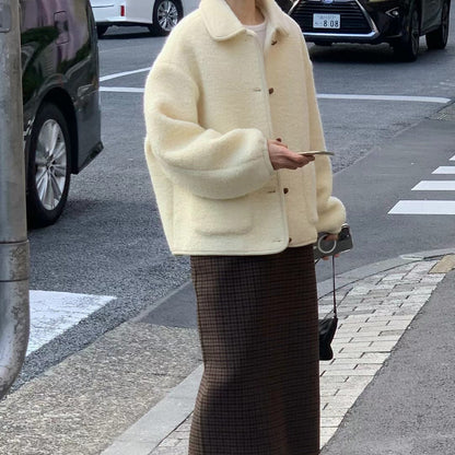 Frau in cremefarbener Teddyjacke und karierter Rock überquert Straße, hält Smartphone. Urbaner Stil, Herbstmode, Straßenmode.