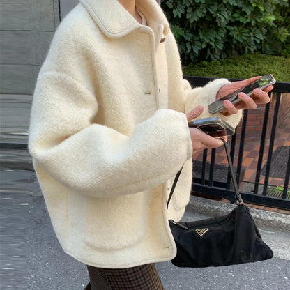 Person in cremefarbener Teddyjacke hält Smartphone und schwarze Prada-Tasche. Modetrend Herbst, Streetstyle, luxuriöse Accessoires.