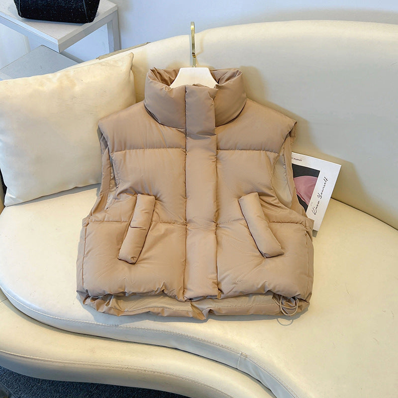Beige Daunenweste auf weißem Sofa, modisch und warm, ideal für Herbst und Winter. Stehkragen, Taschen, stilvolles Design für Damenmode.