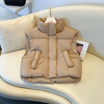 Beige Daunenweste auf weißem Sofa, modisch und warm, ideal für Herbst und Winter. Stehkragen, Taschen, stilvolles Design für Damenmode.