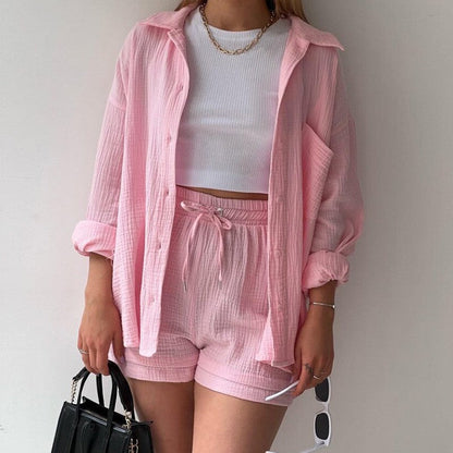 Frau in rosa Leinen-Set mit Hemd und Shorts, weißem Top, Kette und schwarzer Tasche. Sommermode, lässiger Stil, trendige Damenbekleidung.