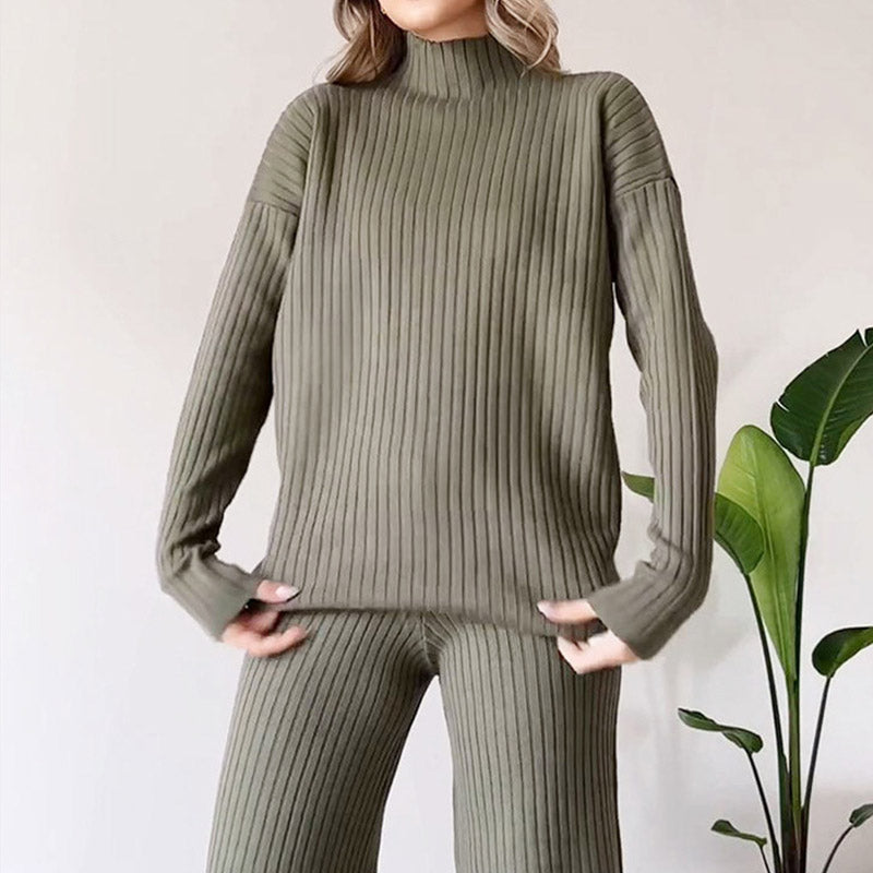 Damen-Outfit aus olivgrünem, geripptem Strickstoff, bestehend aus langärmligem Pullover und passender Hose, vor neutralem Hintergrund mit Pflanze.