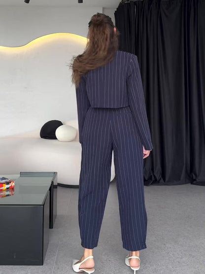 Frau in gestreiftem Anzug von hinten, moderne Inneneinrichtung, schwarze Vorhänge, stilvolle Mode, elegantes Design, zeitgenössischer Look.