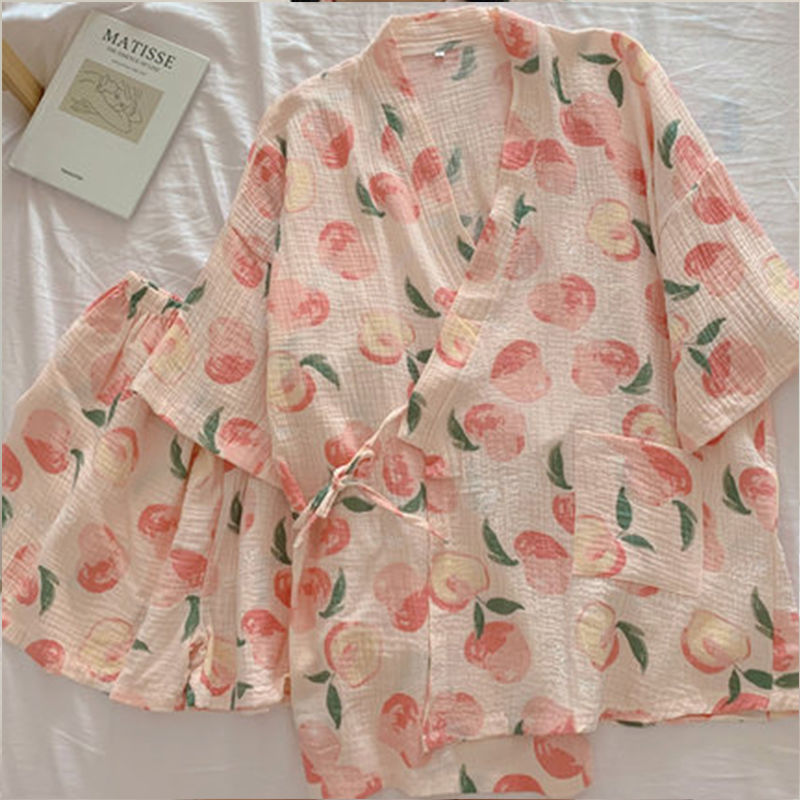 Rosa Kimono mit Pfirsichmuster auf weißem Hintergrund, neben einem Buch. Leichte, sommerliche Damenmode, ideal für entspannte Tage.