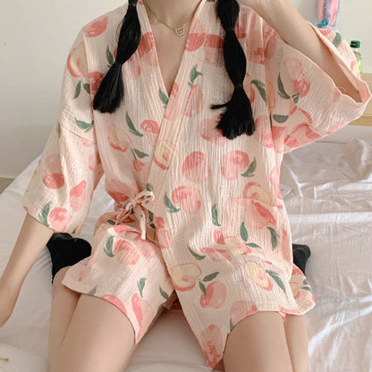 Person in einem pfirsichgemusterten Kimono sitzt auf einem Bett. Der Kimono hat kurze Ärmel und einen Bindegürtel. Ideal für Sommermode und Freizeitkleidung.