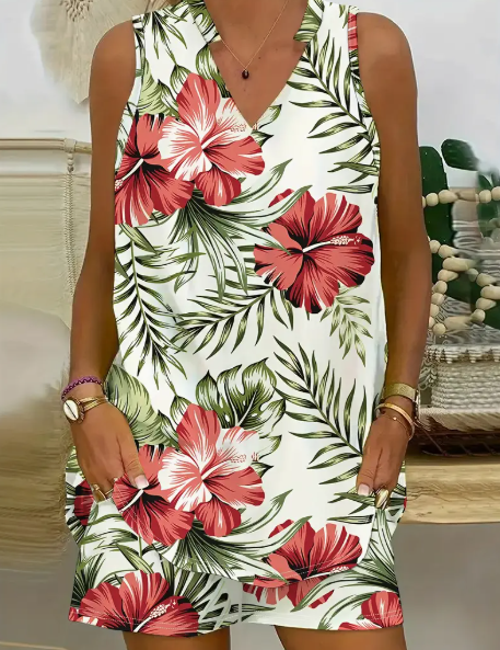 Frau in ärmellosem Sommerkleid mit tropischem Blumenmuster, rote Hibiskusblüten und grüne Blätter, modisch, lässig, ideal für Strandurlaub.