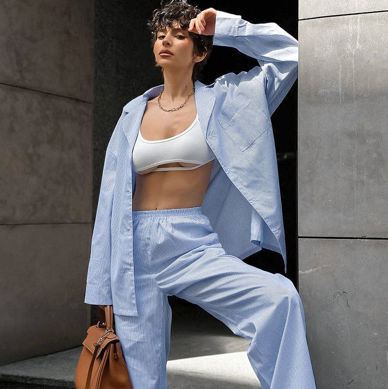 Frau in blauem Anzug und weißem Top posiert modisch mit brauner Tasche. Stilvolle Damenmode, lässiger Look, urbane Kulisse.