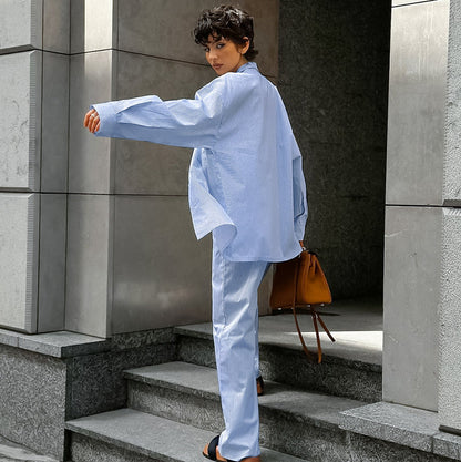 Frau in hellblauem Anzug mit brauner Tasche auf Treppe, moderne Architektur, stilvolle Mode, urbaner Look, Rückansicht.