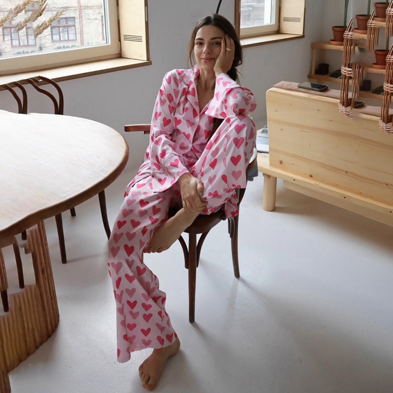 Frau in rosa Pyjama mit Herzmuster sitzt entspannt auf einem Stuhl in modernem Wohnzimmer. Gemütliche Morgenroutine, Innenraum, Entspannung.