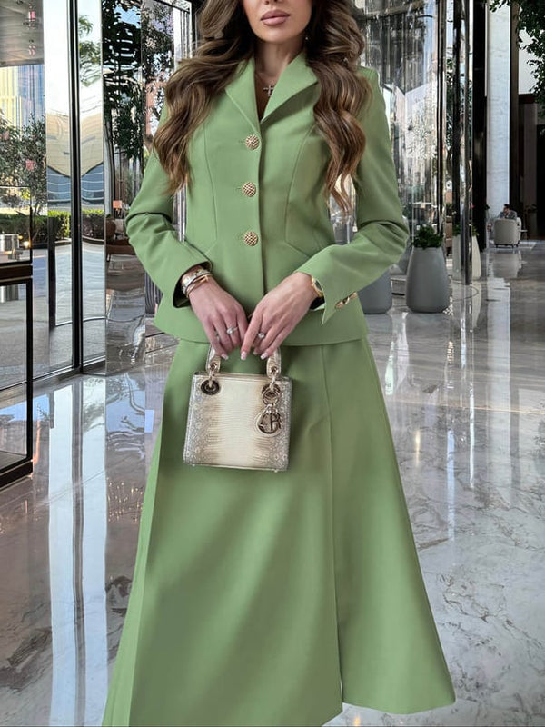 Frau in eleganter, grüner Anzugjacke und Rock, hält eine goldene Designer-Handtasche. Luxuriöse Hotellobby im Hintergrund. Fashion, Stil, Mode.