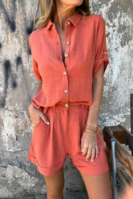 Frau in orangefarbener Leinenbluse und Shorts vor rustikaler Wand. Sommermode, lässiger Stil, Damenbekleidung, Freizeitoutfit.
